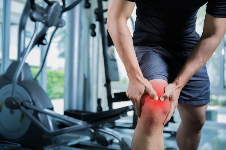Person holding knee in pain with gym equipment in background